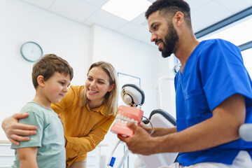 Obraz premium Young multiracial dentist showing little boy how to clean teeth, concept of children oral hygiene,prevention and dental health.