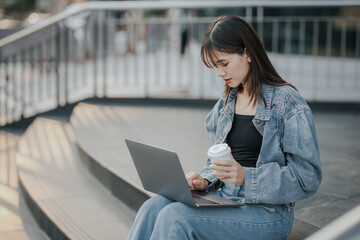 Young Asian woman in jeans using a laptop in the city.