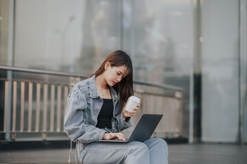 Young Asian woman in jeans using a laptop in the city.