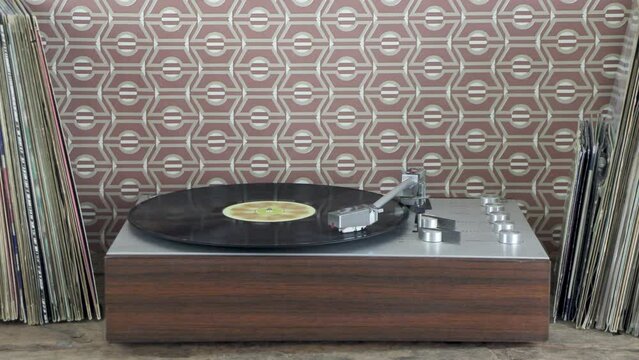 Vintage record player in front of retro brown wallpaper with stacks of vinyl records