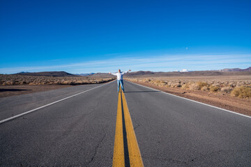 Older man standing in the middle of a desert road with arms outstretched. High quality photo - Powered by Adobe