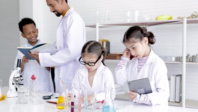 Asian adorable student wearing white gown making experiment with professional man in a chemistry classroom, teacher man teaching kids mix the solution in lab. happy education concept.