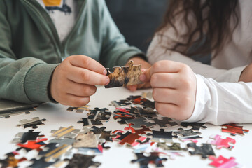 Brother and sister playing puzzles at home. Children connecting jigsaw puzzle pieces in a living...
