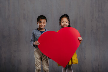 Fototapeta na wymiar Studio shoot of little boy and girl holding model of heart.