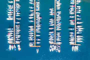 Aerial view of yachts and motorboats moored in a port with clear blue water in summer. Top view from drone of sailboats and various speed boats in dock