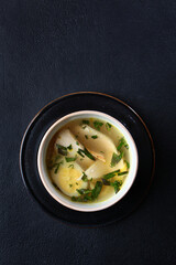 Fresh fish soup in a bowl on a black background, top view. White fish soup. Transparent broth. A...