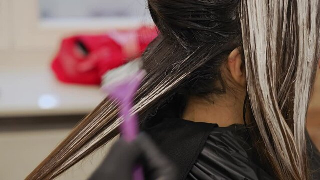 Dark haired woman getting hair coloured in a beauty salon highlighting procedure. High quality 4k footage