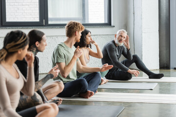 Middle aged coach explaining nostril breathing to multiethnic group in yoga class.