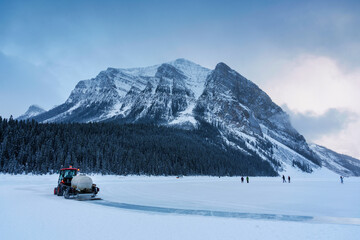 Fototapeta na wymiar Tractor plowing snow on frozen lake preparing for natural ice rink in Lake Louise in the morning at Banff national park