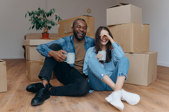 Couple moving in house. interracial couple sitting on the floor near cardboard boxes and drinking tea - Powered by Adobe