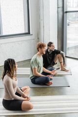 Young smiling multiethnic people talking on mats in yoga class.