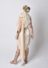 Full length portrait of beautiful blonde woman wearing a fantasy goddess toga costume with  magical crown.
Standing pose, facing backwards away from camera.  isolated on white studio background.