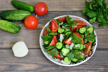 A bowl of salad with onion tomato and cucumbers on a wooden table isolated