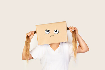 Mujer con caja de cartón en la cabeza y gesto de enfado y tirándose del pelo sobre un fondo gris claro. Vista de frente y de cerca. Copy space
