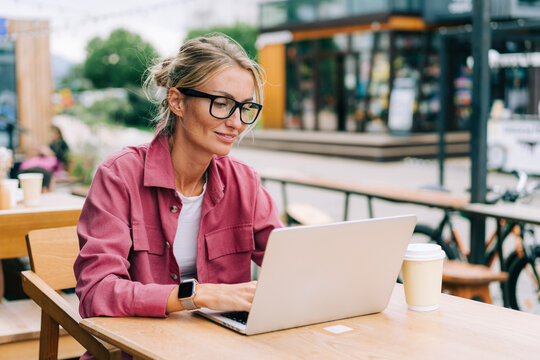 Young blonde business woman sitting on the terrace in a cafe working on a laptop.