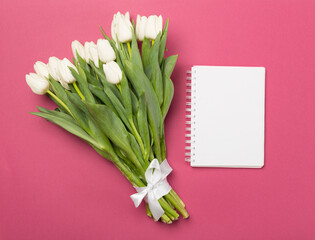 White tulip bouquet with notebook on color background, top view