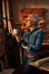 Joyful female carpenter having coffee in workshop.