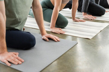 Cropped view of people doing Half Pigeon asana on mats in yoga class.