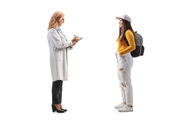 Full length profile shot of a female student standing and talking to a female doctor writing a document