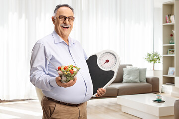 Mature man holding a salad and a weight scale at home
