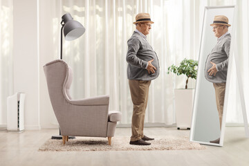 Elderly man with a big belly standing in front of an armchair and looking at a mirror