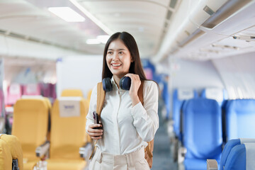 Young asian attractive woman travel by airplane, Passenger wearing headphone putting hand baggage...