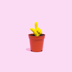 Bright yellow pointer symbol icon growing from a small pot on a pastel pink background. Hand gesture, attention or essence concept.