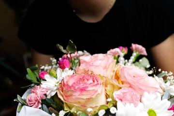Florist woman holding a beautiful blossoming flowers bouquet in pink and green colors of roses, peony, myrtle, pistachio leaves. Woman get present beautiful flowers composition. Out of focus