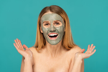 positive woman with red hair and clay mask on face smiling isolated on turquoise.