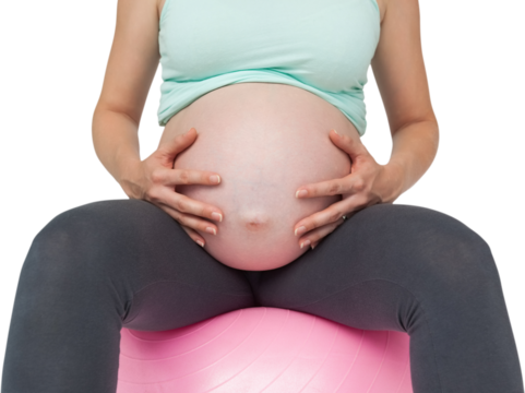 Pregnant woman sitting on pink exercise ball holding her bump