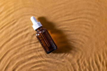 Glass bottle with serum or oil cosmetic product on a shiny water background. Top view, mock up.