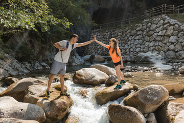 Young couple of hikers successfully crossing rocky river terrain, giving high five to each other. Extreme hike concept.