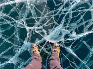 A foot of tourist standing on the cracks surface of frozen lake Baikal in the winter season of...