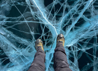 A foot of tourist standing on the cracks surface of frozen lake Baikal in the winter season of...
