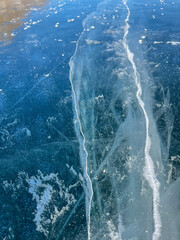 The natural texture of winter ice with white bubbles and cracks on a frozen lake. Abstract background of ice and cracks on the surface of frozen Lake Baikal