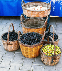 Wicker baskets full of green and black olives standing outdoor on paving stones. Street food market in Turkey.