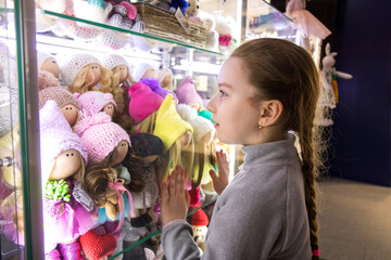 little cute girl looks with admiration at handmade dolls in a shop window