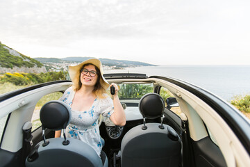 Woman in summer hat driver holding car keys driving her new car cabriolet - automobile and purchase concept
