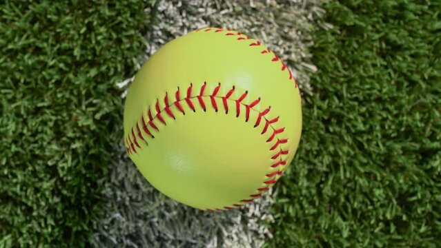 An overhead close-up shot of a softball sitting on the foul line of the outfield grass as the camera rotates – fast.