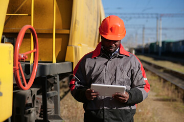 Inspector of wagons at freight train station looks in tablet computer