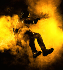 Silhouette of police officer in tactical gear descending from a height, rope exercises with weapons. Tactical rappelling, anti-terror or counter terrorism operation in darkness in rappelling harness