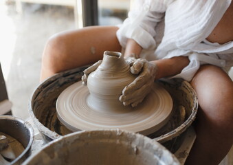 A young ceramist woman sits behind a potter's wheel, Handicraft