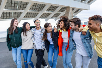Obraz premium Diverse happy student community friends laughing together outdoors. Cooperation concept with millennial people hugging each other showing teamwork and friendship.