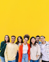 Happy young group of teenage people smiling at camera standing over yellow background. Diverse student friends showing unity and community embracing each other. Copy space for text