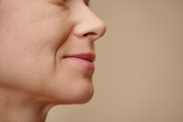 Face of middle-aged woman with nasolabial folds, isolated on beige