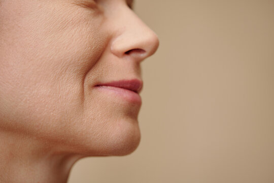 Face of middle-aged woman with nasolabial folds, isolated on beige