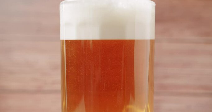 Craft Beer into the large glass. Beer Mug. On a wood background. Half a liter, close up. Rotation 360 degrees. Glass full of beer.
