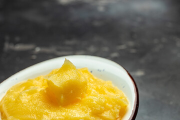 Pure OR Desi Ghee also known as clarified liquid butter in a bowl with wooden spoon on a dark background. Long banner format