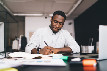 Concentrated African American male writing notes in notebook