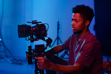 African American operator concentrating on his work, he using camera on the set - obrazy, fototapety, plakaty
